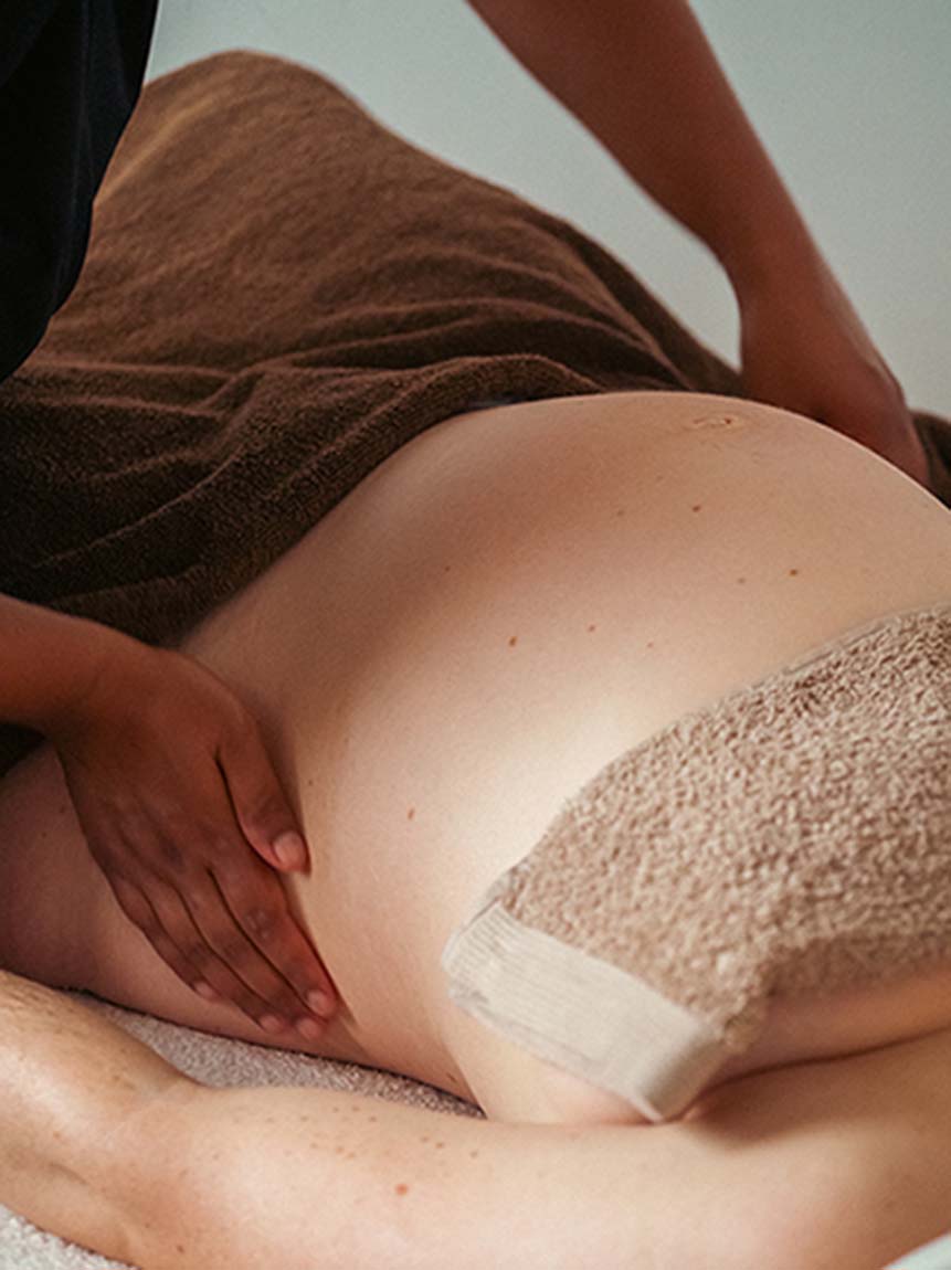 Une femme enceinte est allongée sur le dos. La masseuse lui masse les hanches pour libérer les tensions