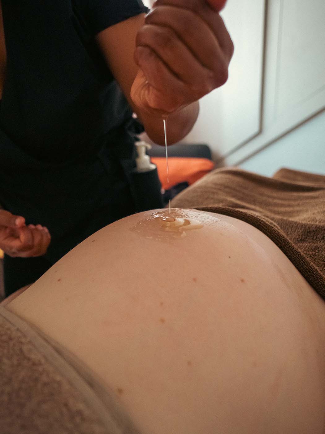 La masseuse verse du creux de sa main de l'huile sur le ventre d'une femme enceinte pour démarrer le massage
